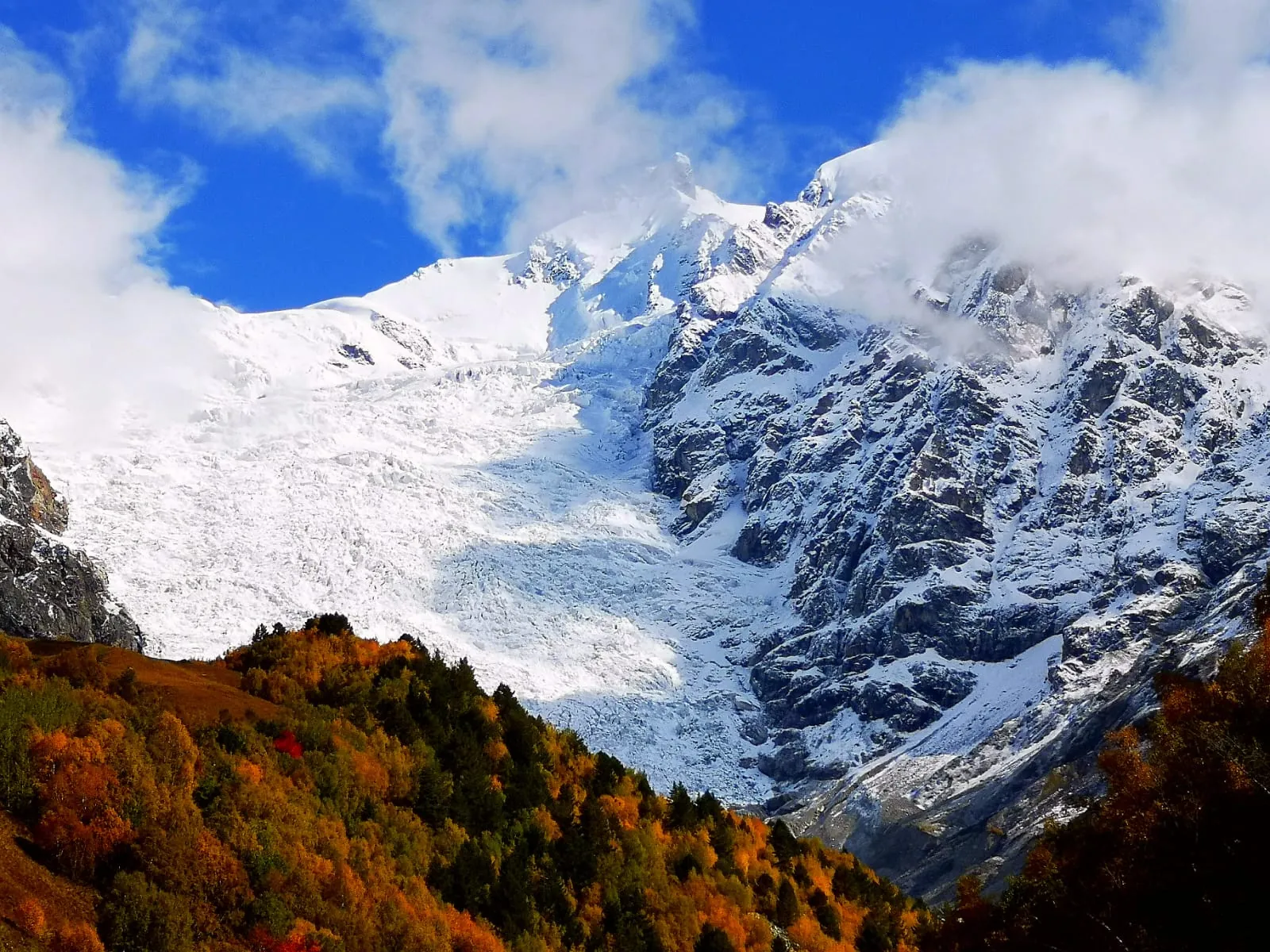 A glacier icefall above an autumn forest