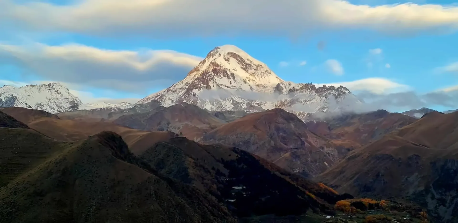Mount Kazbek in golden light above the autumn hills of Stepantsminda